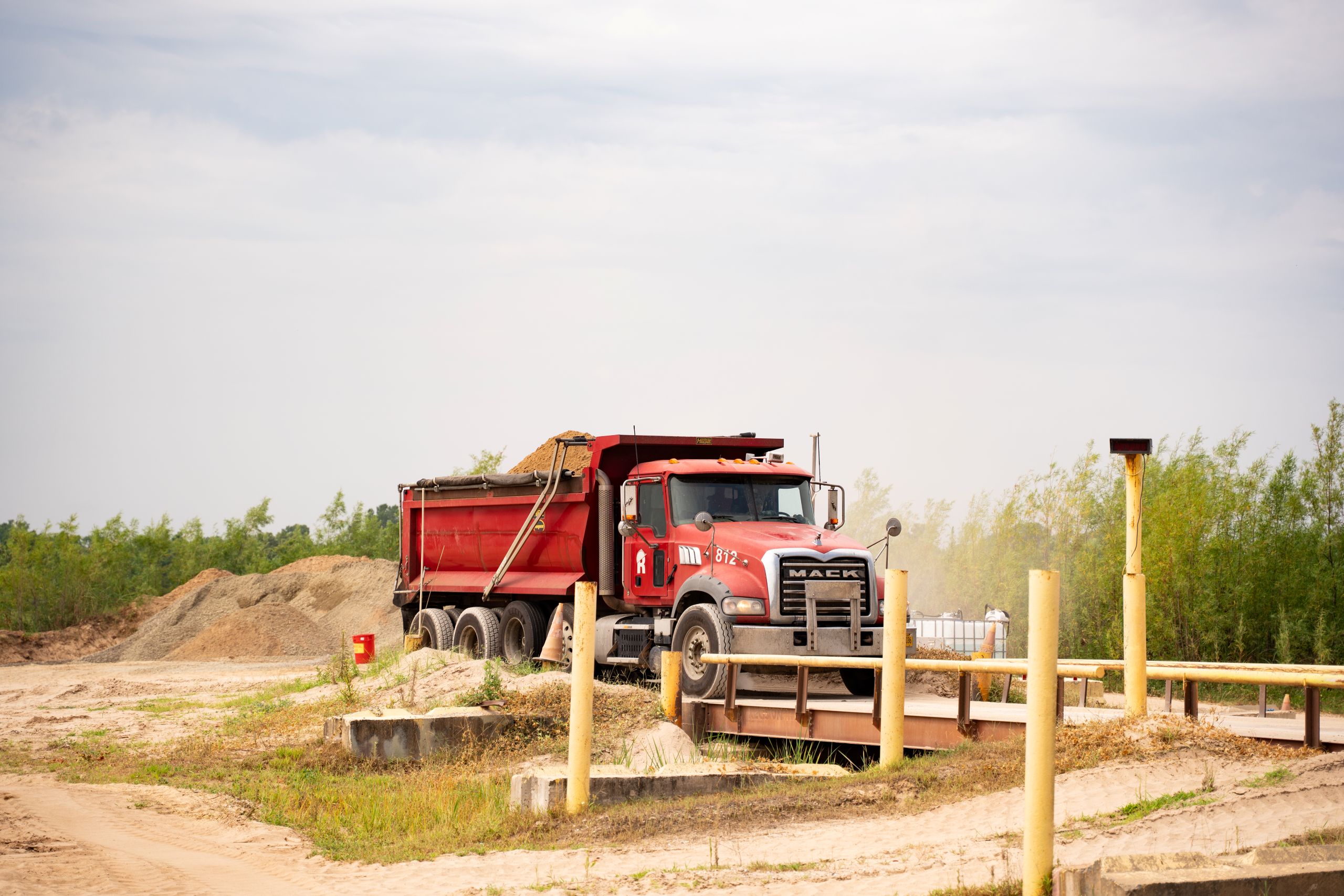 A red Mack dump truck carrying a load of soil drives across a bridge at a construction site.